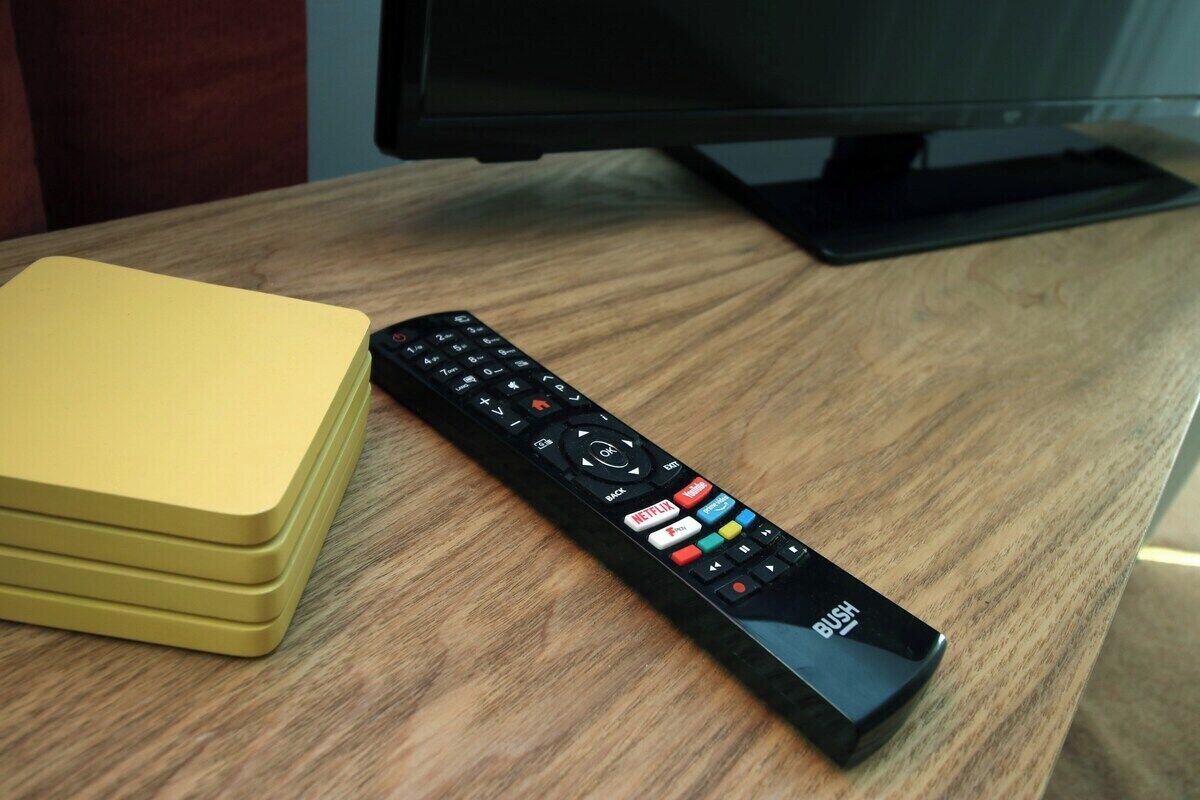 A remote control on a wooden table with a yellow object beside it.