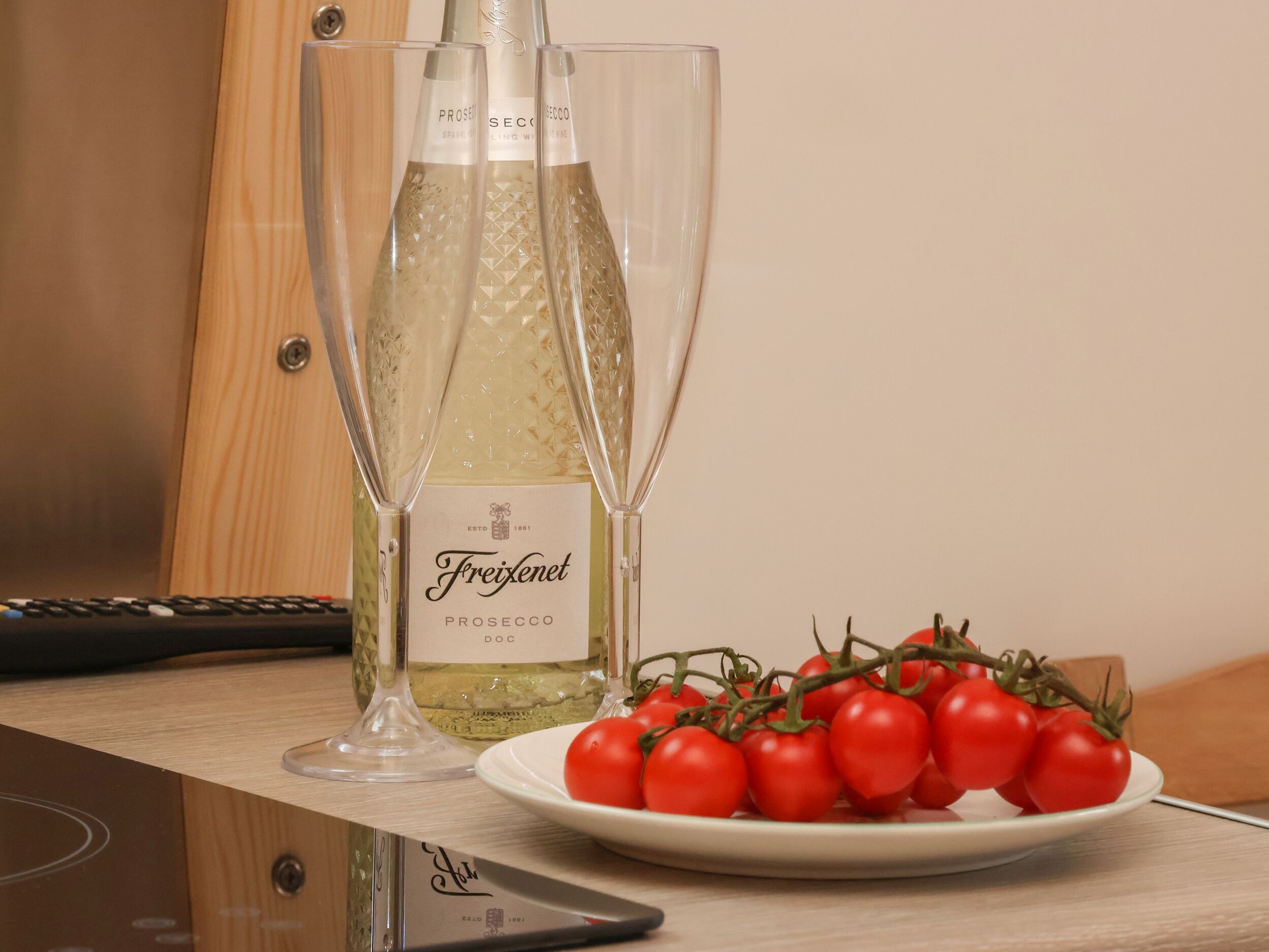 A bottle of Freixenet Prosecco DOC wine, two glasses, and a plate of tomatoes on a wooden surface.