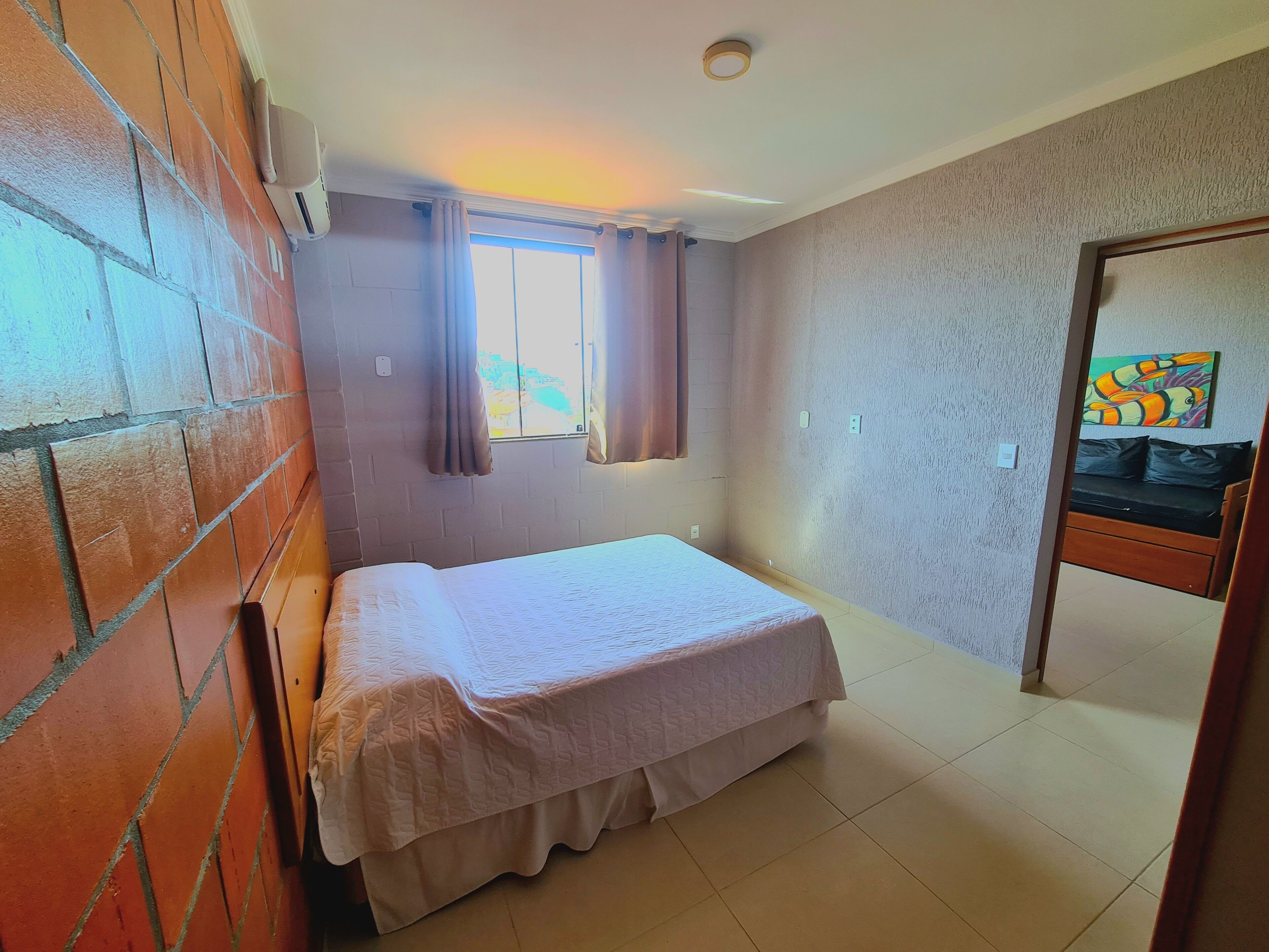 A room with a bed, a window with curtains, a brick wall, and a painting on the wall.