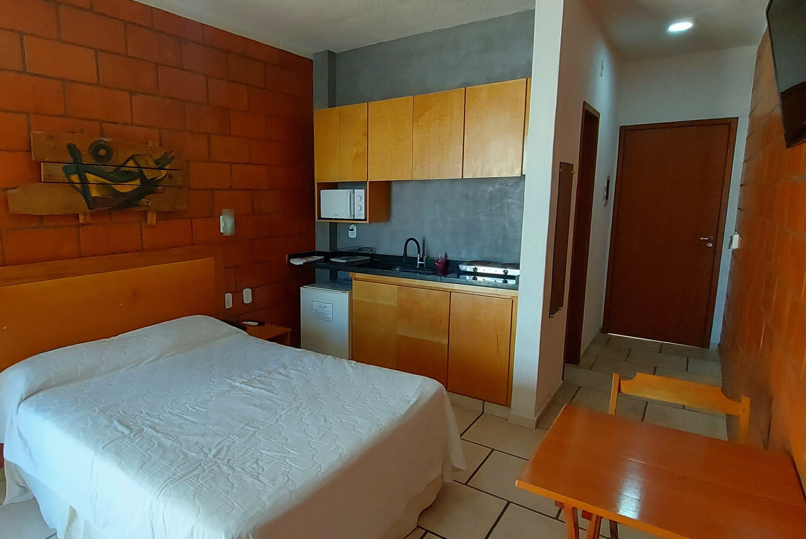 A compact hotel room with a bed, a small kitchenette, a microwave, and a wooden cabinet.