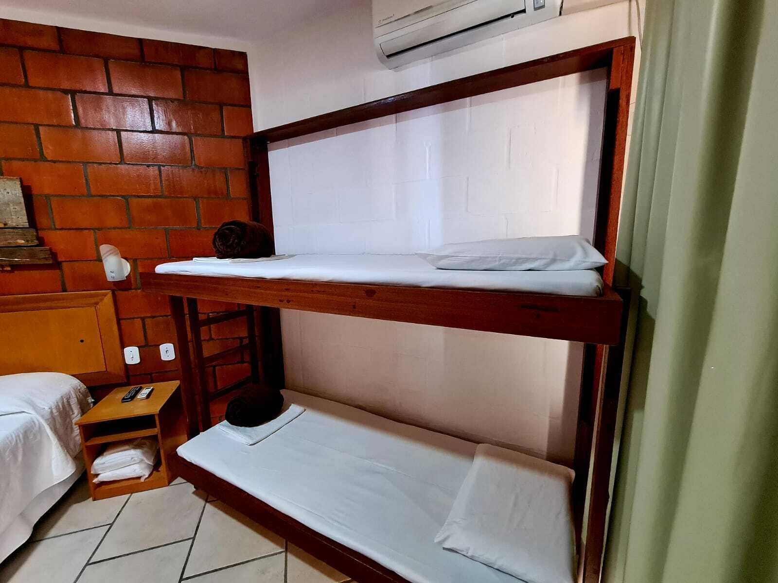 Une chambre avec un lit superposé, un mur en briques, une petite table en bois et un matelas blanc sur le lit du bas.