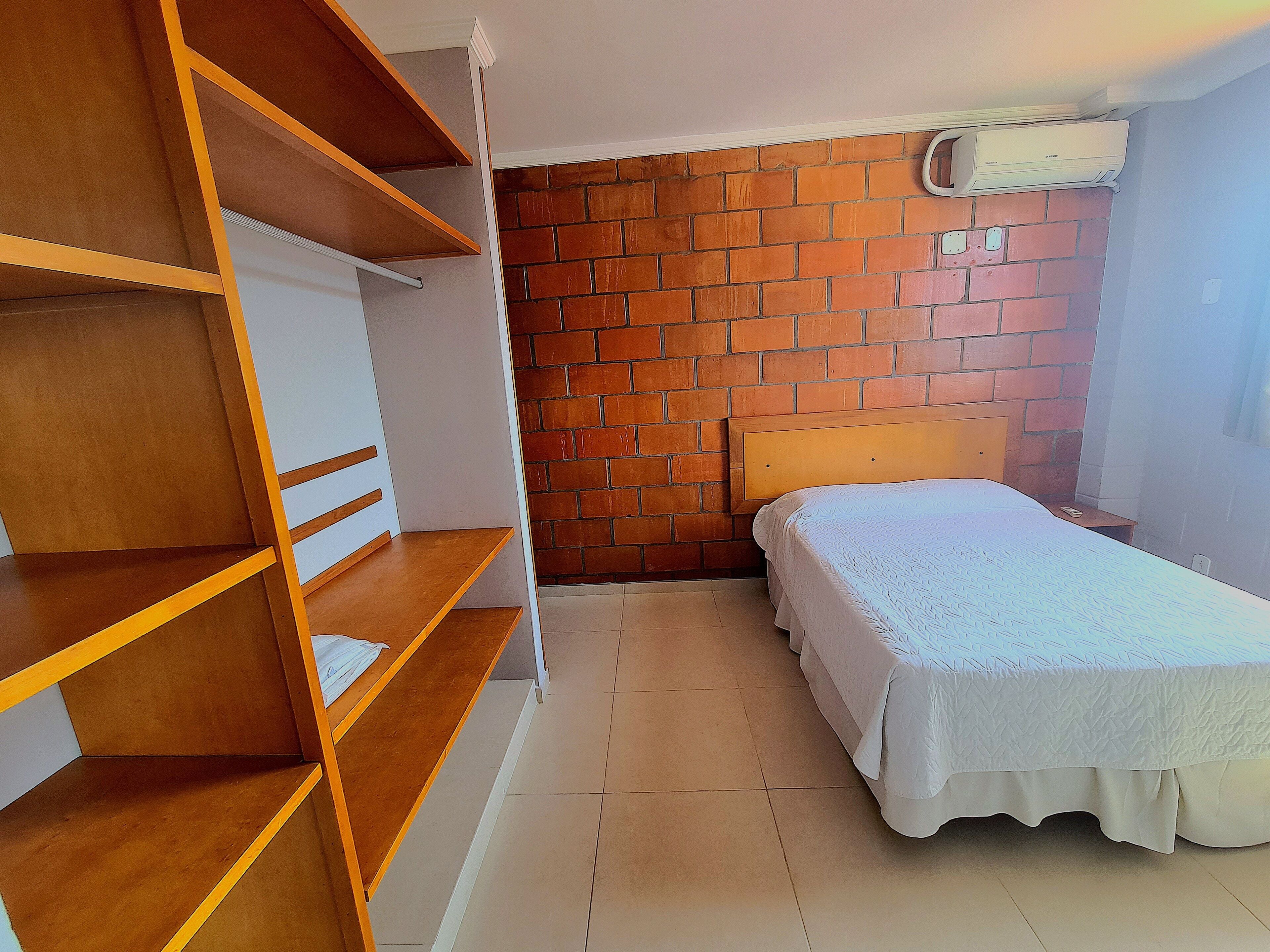 Una habitación con una cama, repisas de madera, una pared de ladrillo y un equipo de aire acondicionado.
