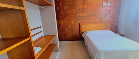 Una habitación con una cama, repisas de madera, una pared de ladrillo y un equipo de aire acondicionado.