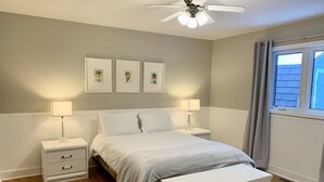 A bedroom with a bed, bedside tables, a ceiling fan, and framed artwork on the wall. - Cottage in the heart of Tobermory - AC & WIFI (Tobermory)
