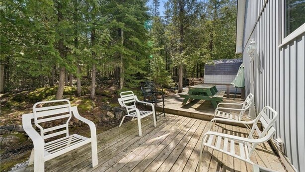 A wooden deck with white metal chairs and a picnic table surrounded by trees. - Cottage in the heart of Tobermory - AC & WIFI (Tobermory)