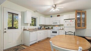 A kitchen with white cabinets, a wooden dining table, and a ceiling fan. - Cottage in the heart of Tobermory - AC & WIFI (Tobermory)