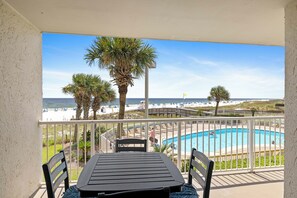 A balcony with a pool, chairs, and a view of the beach and ocean.