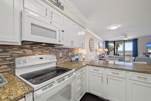 A modern kitchen with white cabinetry, a built-in microwave, a stove with a digital clock, and a granite countertop.