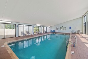 Una piscina interior con agua cristalina, rodeada de sillones de descanso y una sombrilla.