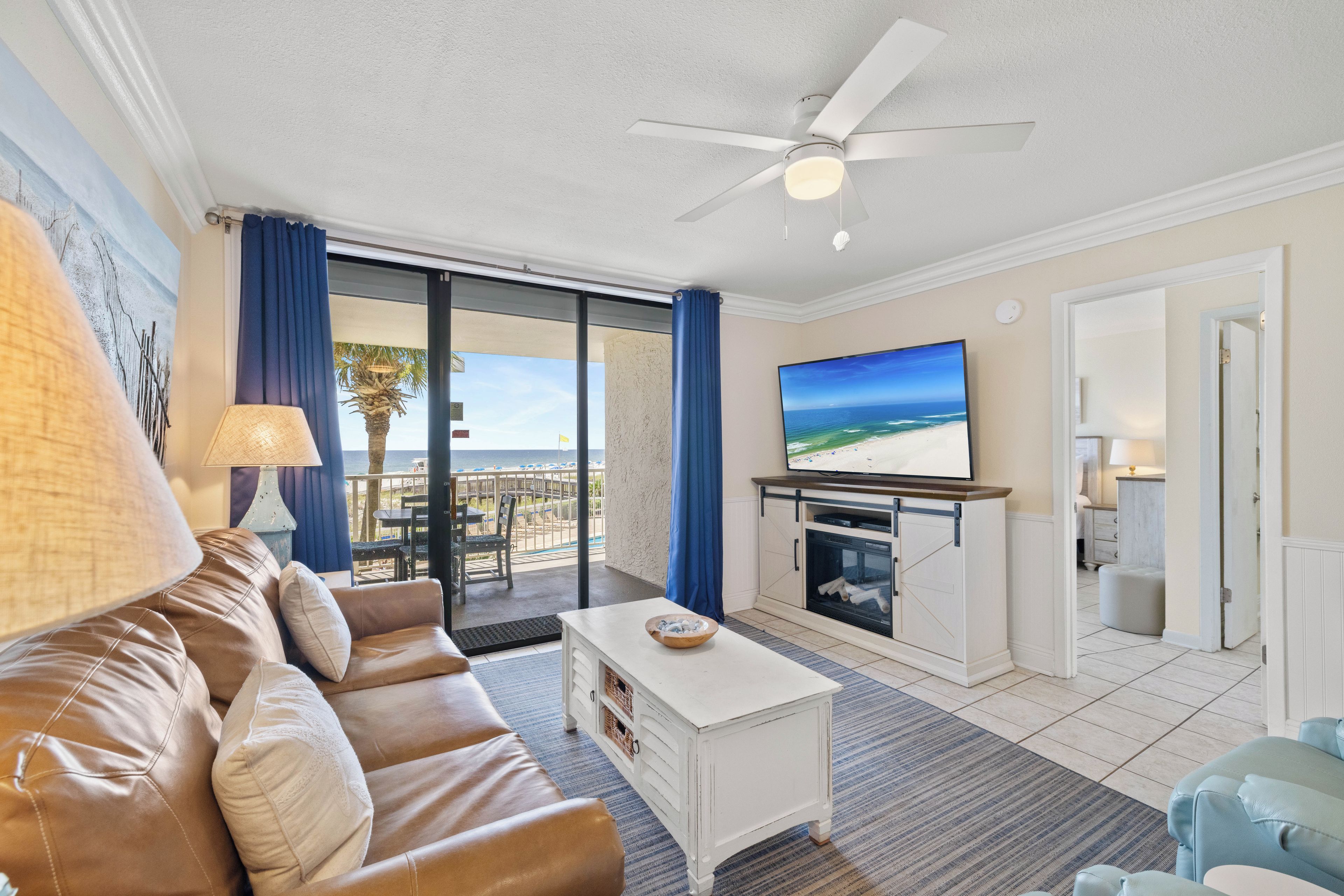 A living room with a sofa, a coffee table, a flat-screen TV, and a ceiling fan.