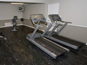 Un gimnasio con dos cintas de correr, una bicicleta estática y una máquina de pesas.