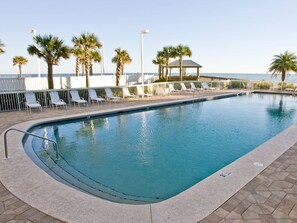 A swimming pool with a curved edge, surrounded by white lounge chairs and palm trees.