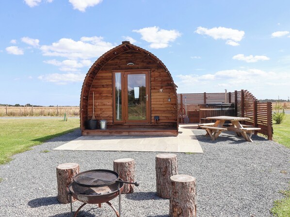 A wooden cabin with a large door, a barbecue grill, and a picnic table.