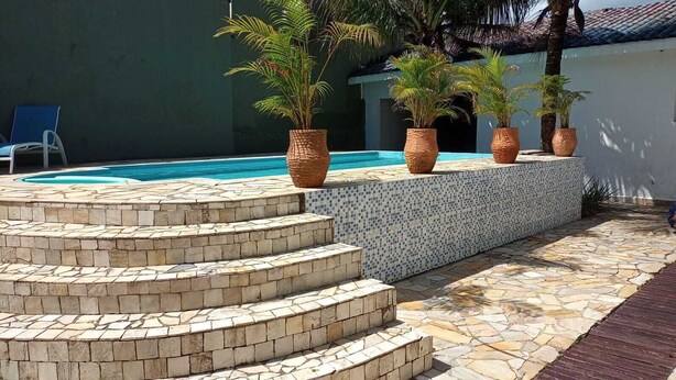 Un espace piscine avec des marches menant à une plateforme carrelée, entourée de plantes en pot et d’une chaise bleue.