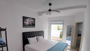 Une chambre à coucher avec un lit, un ventilateur de plafond, un tableau encadré accroché au mur et une porte donnant sur un balcon.