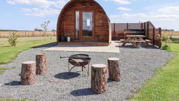 Una baita di legno con tetto curvo, una porta e una finestra. Davanti alla baita, un tavolo da picnic e un barbecue.