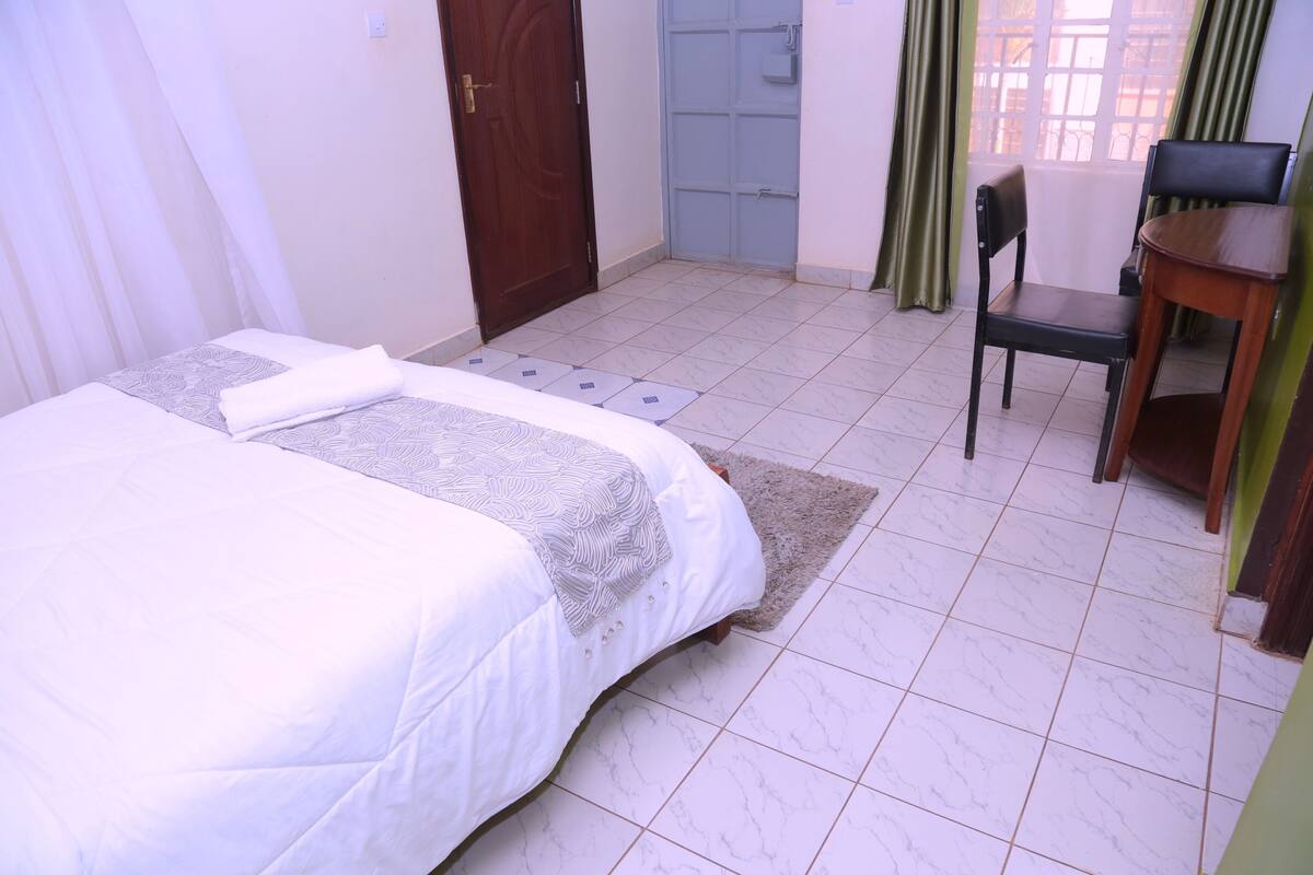 A bedroom with a bed, a desk, a chair, a door, and a window.