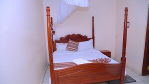 Una cama con dosel y un cabecero de madera, ropa de cama blanca y almohadas a rayas.