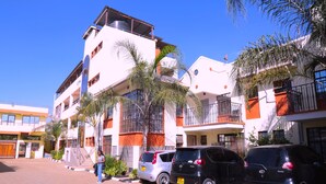Un edificio de varios pisos con un gimnasio en la planta baja, rodeado de coches aparcados y palmeras.
