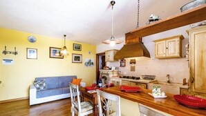 Une cuisine avec des meubles en bois, une table à manger avec des chaises et un mur jaune orné de tableaux.