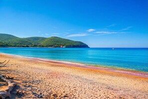 A beach with clear blue water, a sandy shore, and green hills in the background. - Casa di Allegra Terme di Venturina (Campiglia Marittima)