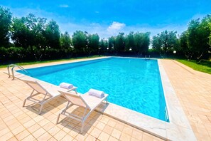 A rectangular swimming pool with clear blue water, surrounded by a tiled deck. There are two lounge chairs with towels on them. - Casa di Allegra Terme di Venturina (Campiglia Marittima)