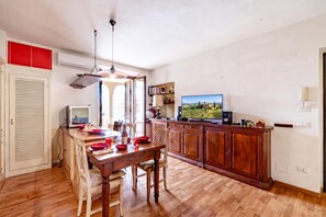 A kitchen with wooden cabinets, a dining table with chairs, a television, and a view of the countryside. - Casa di Allegra Terme di Venturina (Campiglia Marittima)