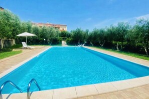 Une piscine rectangulaire à l’eau d’un bleu limpide, entourée d’une terrasse carrelée. On y trouve des chaises longues et un petit parasol.