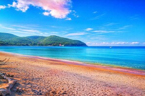 A beach with clear water, a sandy shore, and a small island with a building. - Casa di Allegra Terme di Venturina (Campiglia Marittima)