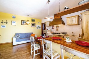 Une cuisine avec des meubles en bois, une table à manger avec des chaises et un mur jaune orné de tableaux.