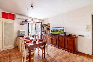 Un coin repas avec une table et des chaises en bois, un téléviseur fixé au mur et un espace cuisine avec des placards et une fenêtre.