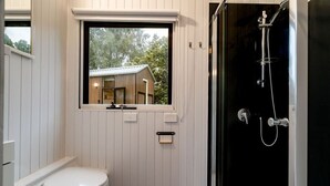 A modern bathroom with a white vanity, a window with a view of a house, and a glass-enclosed shower. - Brumbys Run by Tiny Away (Warragul South)