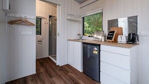 A compact kitchen with white cabinetry, a built-in dishwasher, a wooden countertop, and a window providing a view of greenery outside. - Brumbys Run by Tiny Away (Warragul South)