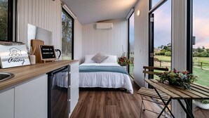 A modern, compact bedroom with a bed, bedside table, and a view of the outdoors. - Brumbys Run by Tiny Away (Warragul South)
