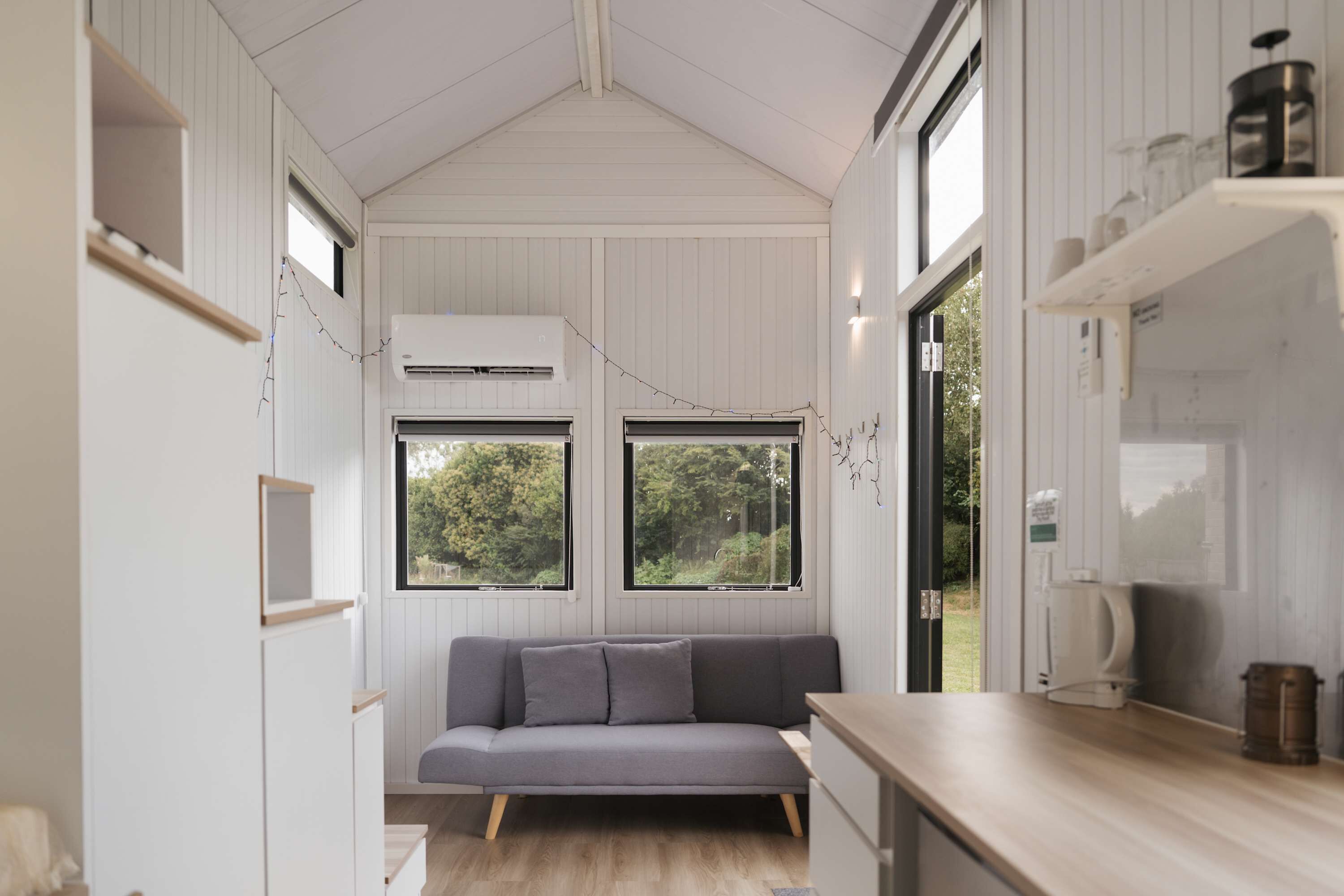 A compact room with a sofa, a wooden counter, and a window with a view of greenery.