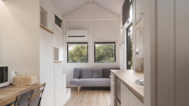 Una cocina compacta con sofá gris, suelo de madera y ventana con vistas a zonas verdes.