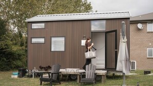 Un edificio pequeño de una sola planta con fachada marrón, una puerta corredera y un pequeño patio con mobiliario exterior.