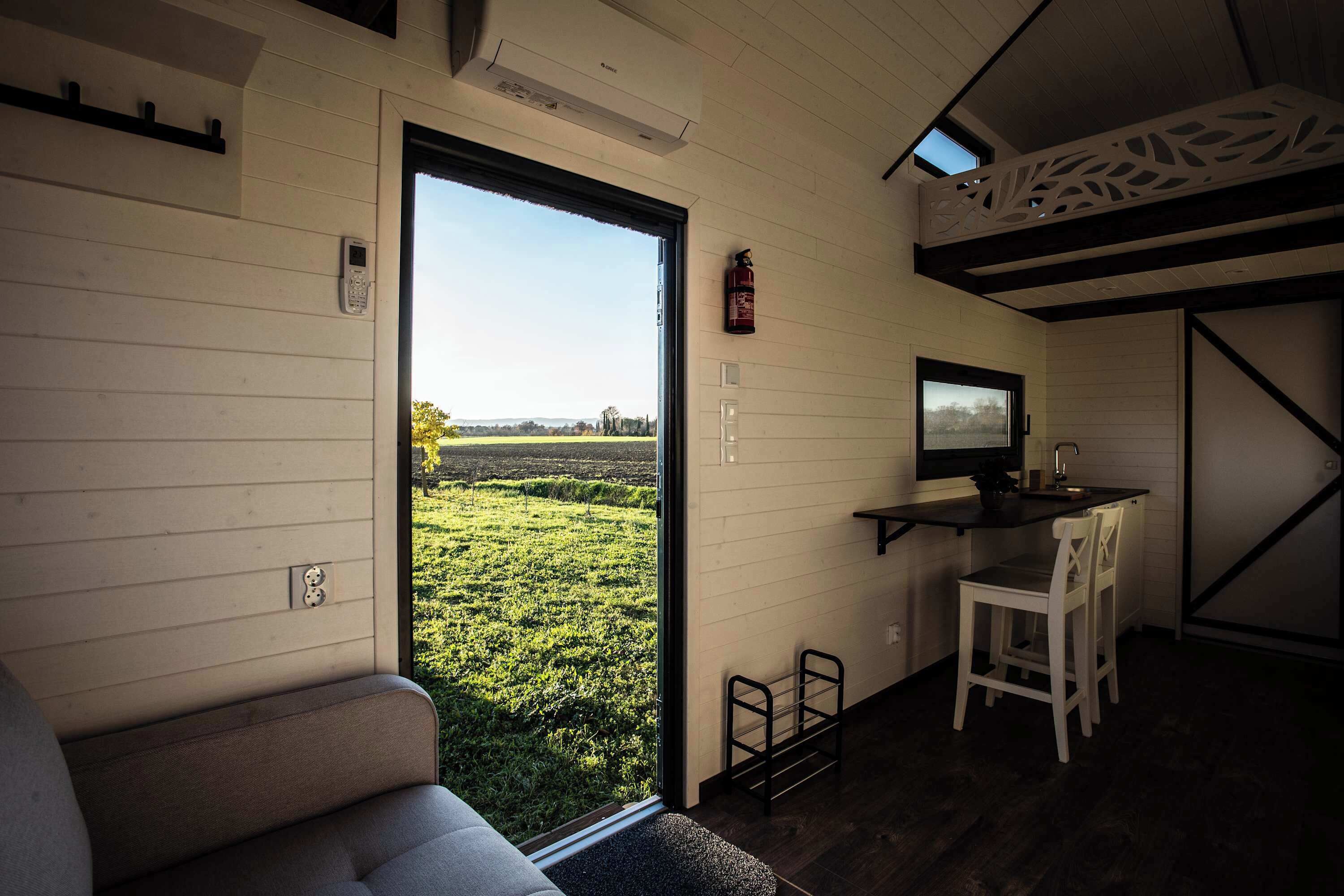 Un interior moderno con un sofá, un pequeño comedor, un televisor y un amplio ventanal con vistas a un campo verde.