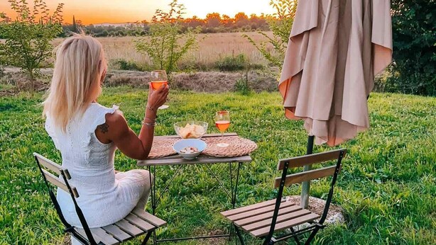 En person sitter vid ett bord utomhus med ett glas att dricka ur, en skål med bröd och ett glas juice.