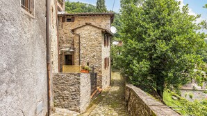 Un étroit sentier de pierres mène à un bâtiment rustique en pierre, doté d’un petit balcon et d’une antenne parabolique.