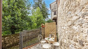 Une terrasse en pierre avec une table et des chaises, une clôture en bois et un bâtiment doté d’un mur en pierre.