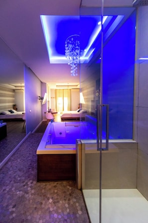A modern hotel room with a glass-enclosed jacuzzi, a bed, a desk, and a large window. - Le Suite del Nostromo (Salerno)