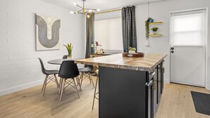 A modern kitchen with a central island, black chairs, a white brick wall, and a hanging light fixture.