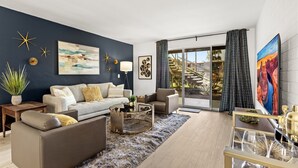 A modern living room with a dark blue accent wall, a large painting, and a view of a staircase.