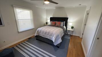 A bedroom with a bed, a ceiling fan, a nightstand with a lamp, and a window with blinds.