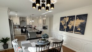 Een moderne keuken met witte kastjes, een centraal eiland en een eetgedeelte met een tafel en stoelen.