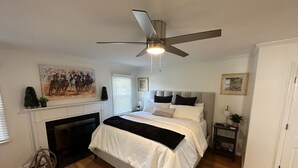 Een slaapkamer met een bed, een plafondventilator, een open haard en een schilderij aan de muur.
