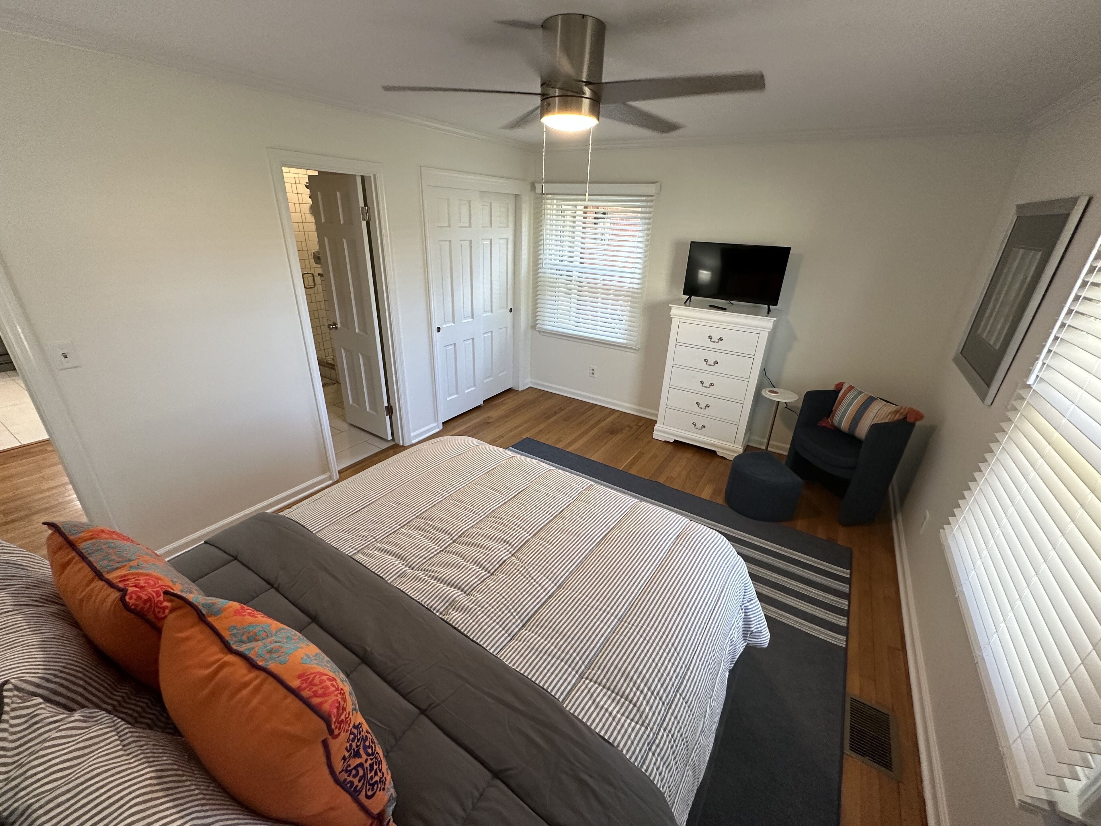 Quarto com cama, cômoda, televisão e ventilador de teto.
