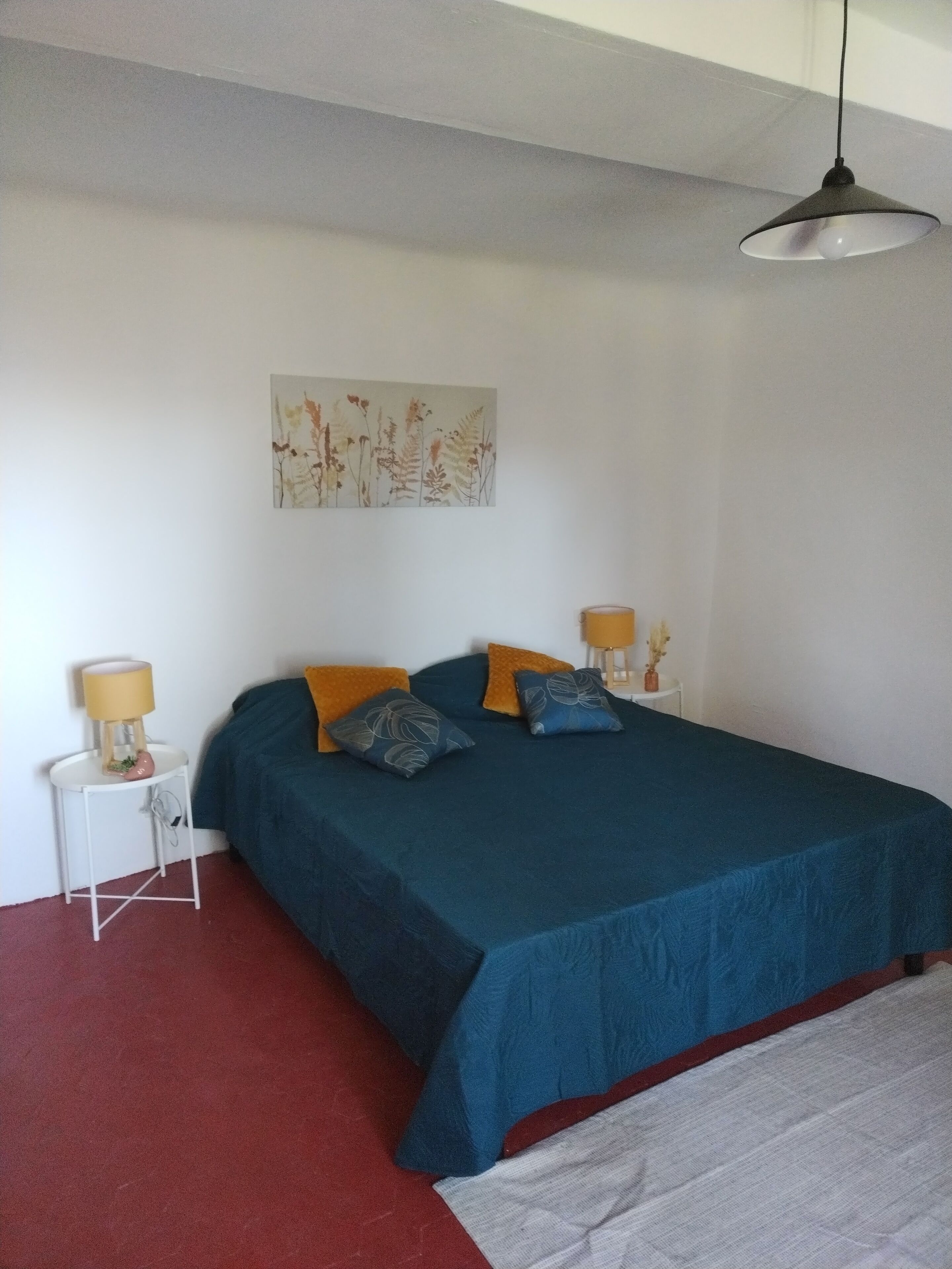 Un dormitorio con una cama, almohadas, una mesita de noche, una lámpara y una obra de arte en la pared.