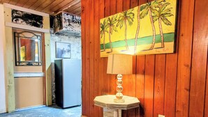 A room with wooden walls, a painting of palm trees, a refrigerator, and a table with a lamp. - Minimalist private studio @ Eau Gallie Downtown, spacious in size of 650 sqft.  (Melbourne)